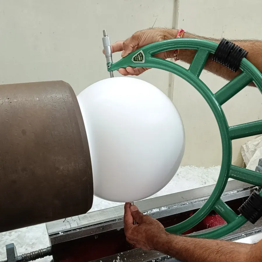 Technician measuring the diameter of a 310 mm PTFE ball with a precision micrometer on a lathe during machining at Hemsun Engg. Industries, Dahegam, Gujarat